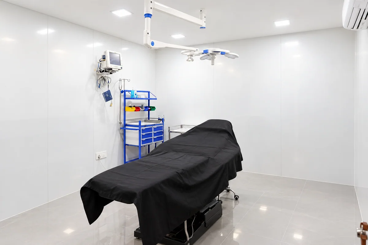Clinical room with a treatment bed, overhead light and equipment trolley